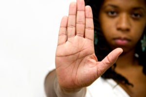 A person with a serious expression standing close to the camera and holding their hand up in a "stop" gesture.