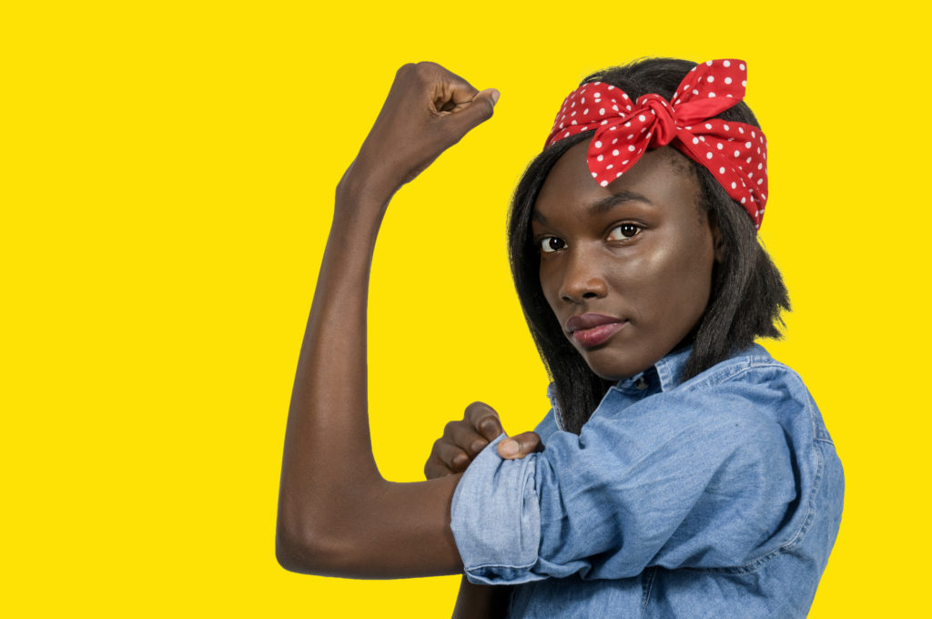 A person dressed as Rosie the Riveter against a yellow background.