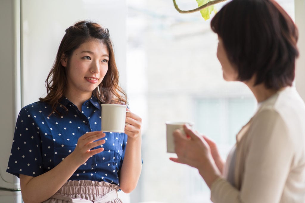 A parent and child holding mugs are talking to each other.