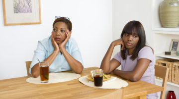 A parent and child look away from each other sadly at the dinner table.