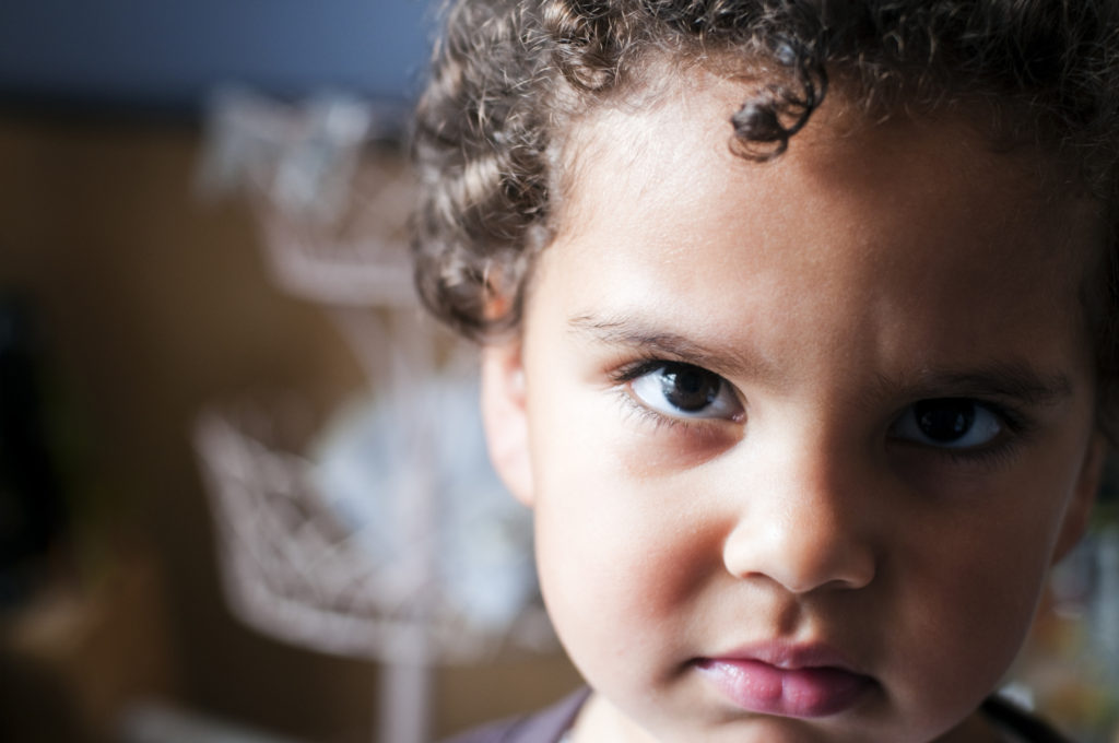 An angry child looks at the viewer; the background is out of focus.
