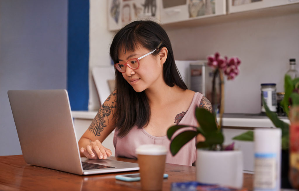 A smiling person looks at their laptop.